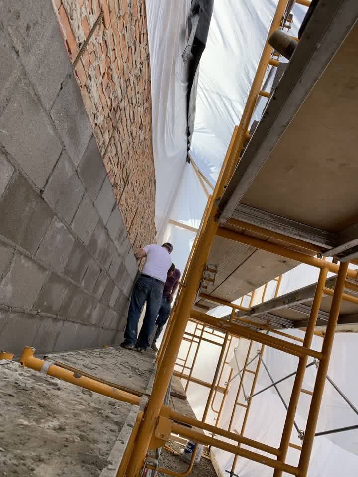 Masons laying block from scaffolding inside the tent
